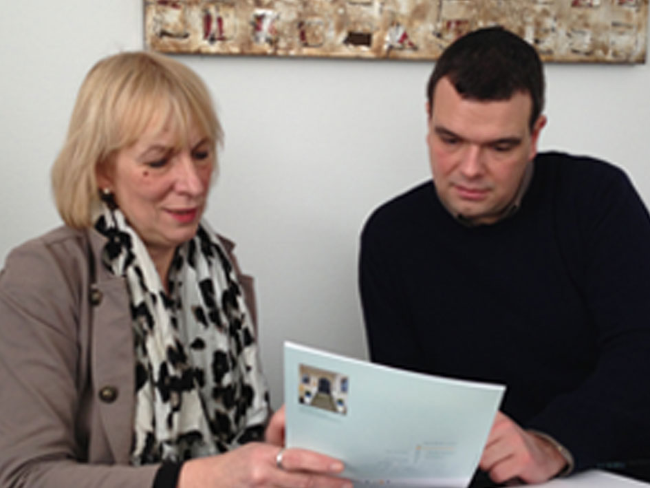 Ein Mann und eine Frau sitzen zusammen und lesen gemeinsam ein Dokument am Tisch.