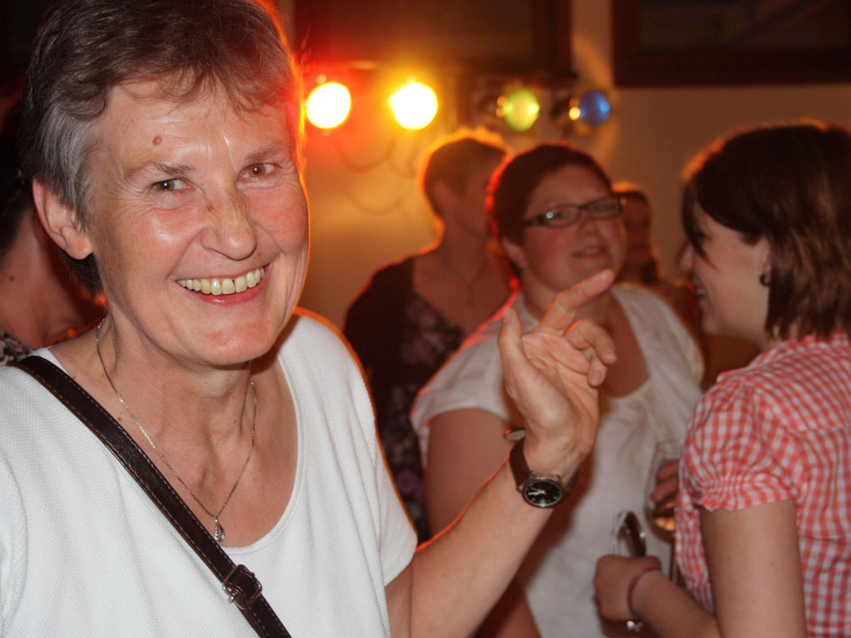 Eine Frau in einem weißen Shirt steht lächelnd vor einem neutralen Hintergrund.