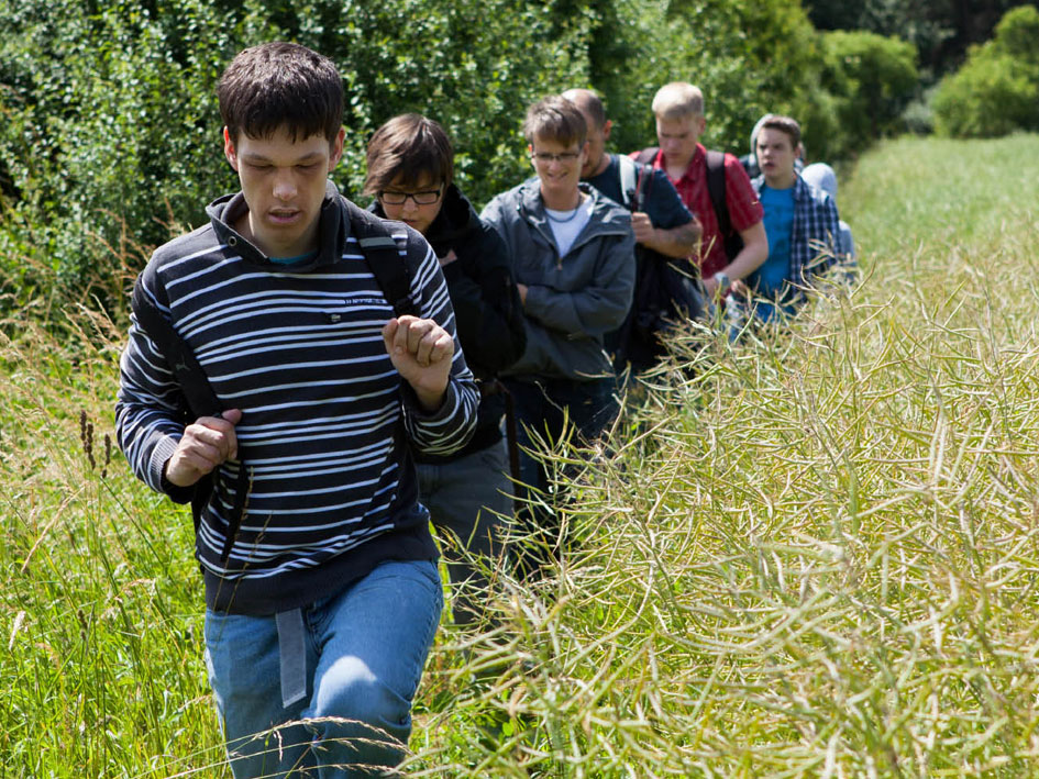 Eine Gruppe von Menschen geht durch ein Feld, umgeben von grüner Vegetation und blauen Himmel.