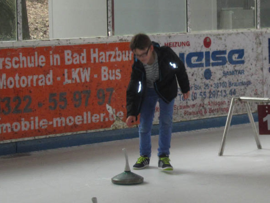 Ein junger Junge spielt Curling auf einer Eisbahn und zielt mit seinem Stein auf das Ziel.