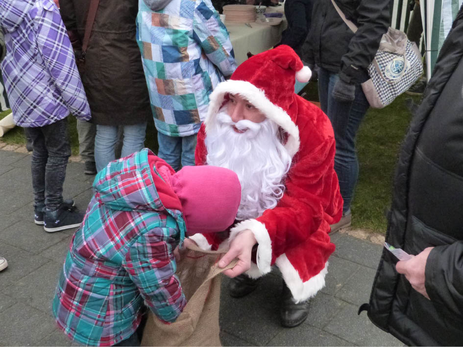 Ein kleines Mädchen überreicht dem Weihnachtsmann eine Tüte mit Lebensmitteln.