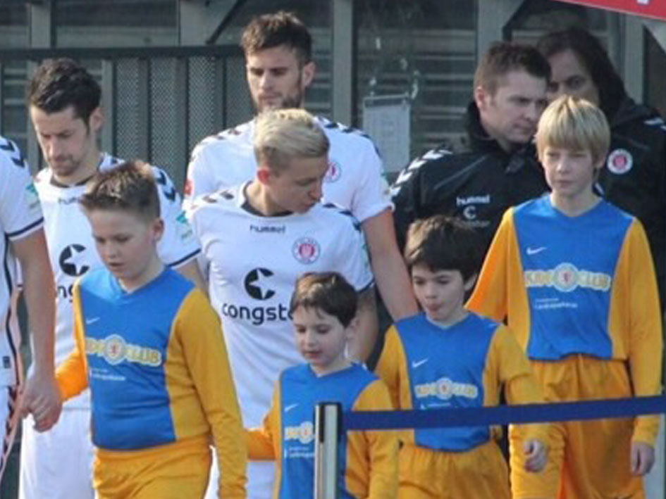 Eine Gruppe junger Fußballspieler steht vor einem Zaun und posiert für ein Foto.