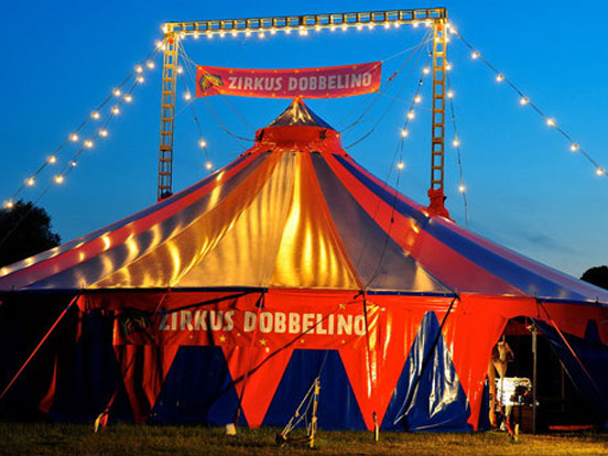 Ein Zirkuszelt, das mit Lichtern geschmückt ist und eine einladende, festliche Stimmung vermittelt.