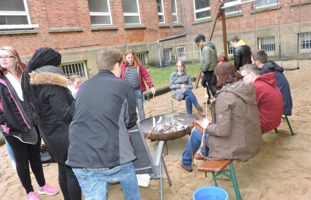 Menschen sitzen entspannt um ein Feuer, das in einem Feuergrube im Freien lodert.