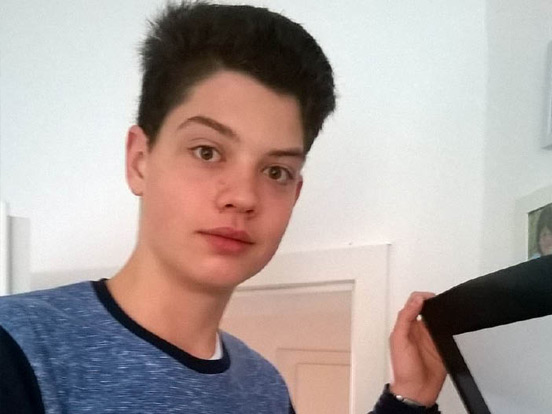 Ein junger Mann hält einen Laptop in der Hand und zeigt den Bildschirm.