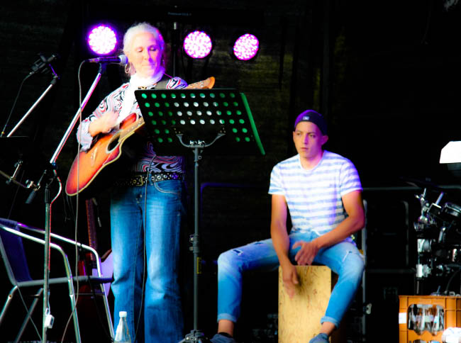 Ein Mann mit einer Gitarre und eine Frau am Schlagzeug treten gemeinsam auf der Bühne auf.