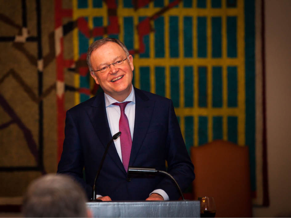 Ein Mann in formeller Kleidung steht an einem Podium und adressiert das Publikum.