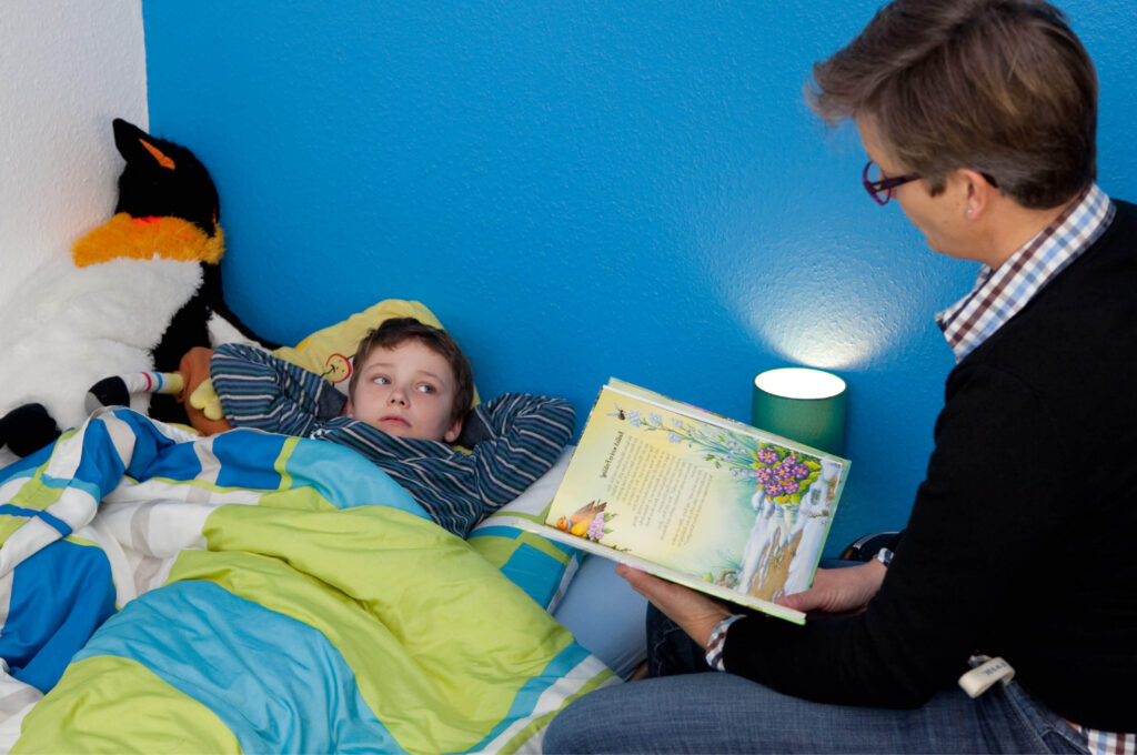 Eine Frau liest einem Kind aus einem Buch vor, beide sitzen gemütlich zusammen.