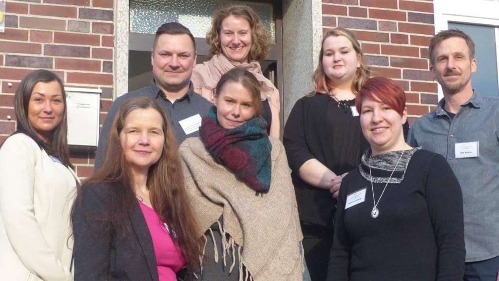 Gruppenfoto von acht Personen vor einem Backsteingebäude. Teamfoto, Mitarbeiterfoto, Firmenportrait.