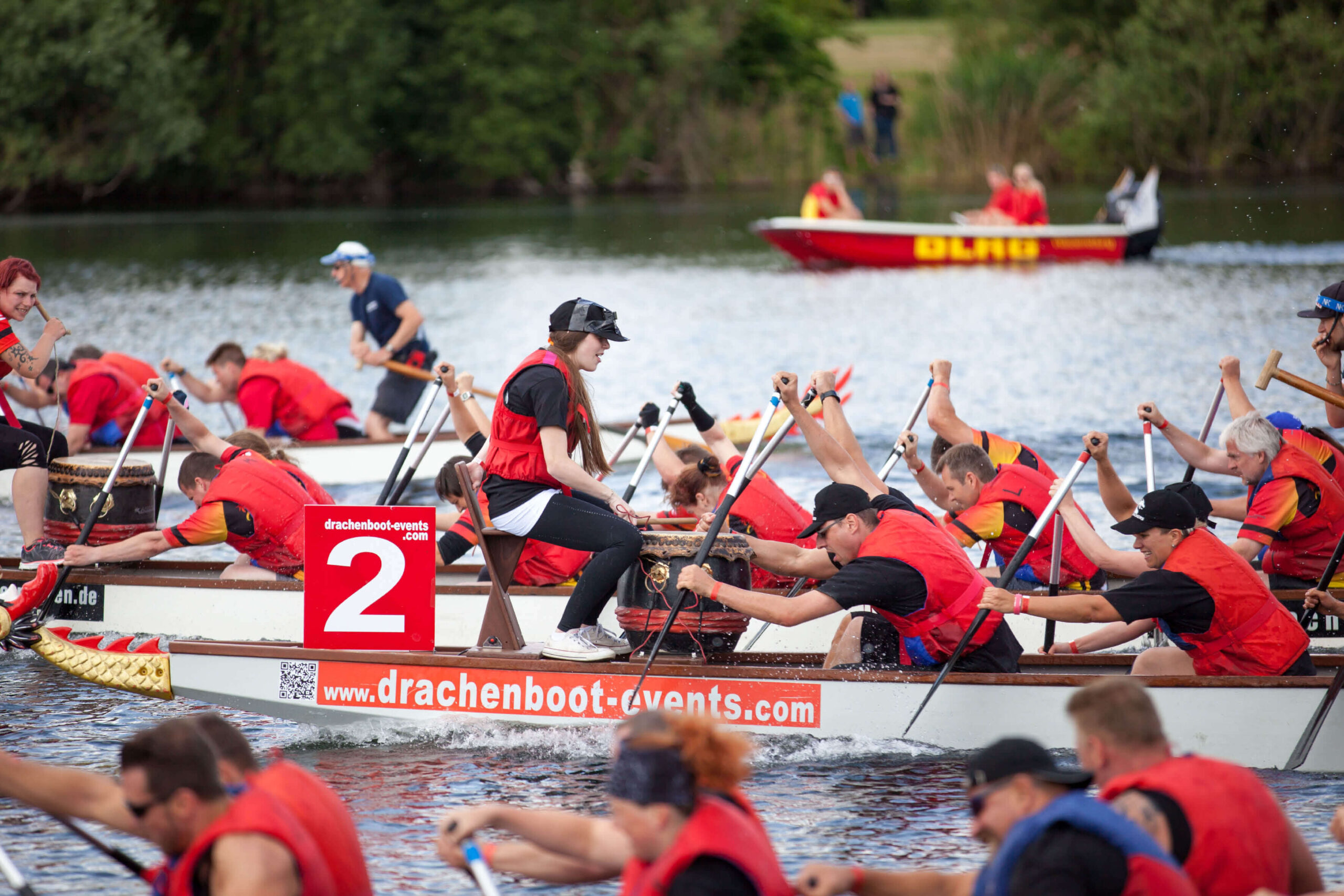 Drachenbootrennen: Team paddelt im Drachenboot auf dem Wasser, Trommler gibt Takt an, DLRG Boot im Hintergrund.