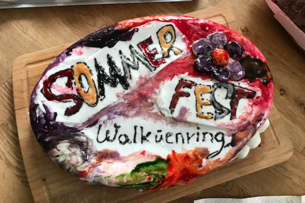 Sommerfest Kuchen Walkürenring, selbstgemacht und kreativ dekoriert mit Blumen und bunter Glasur auf Holzbrett.