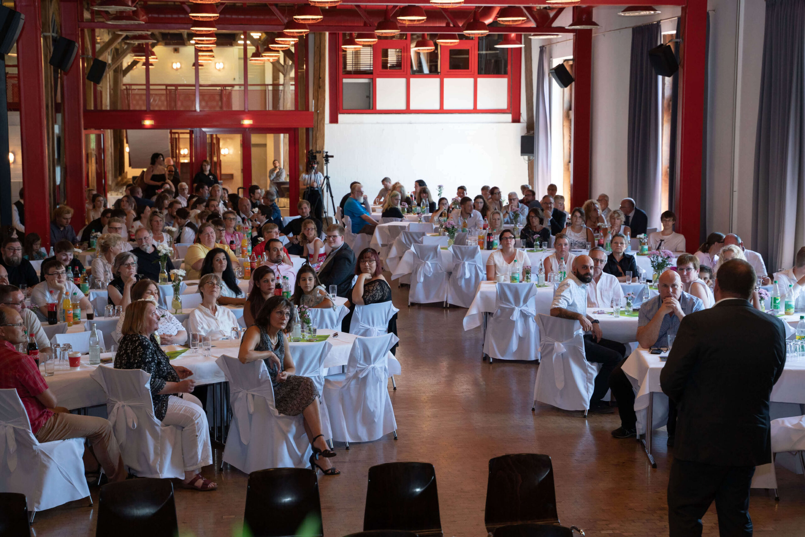 Große Festgesellschaft bei Veranstaltung in Halle. Menschen sitzen an Tischen, hören Rede zu. Hochzeit, Jubiläum, Event.