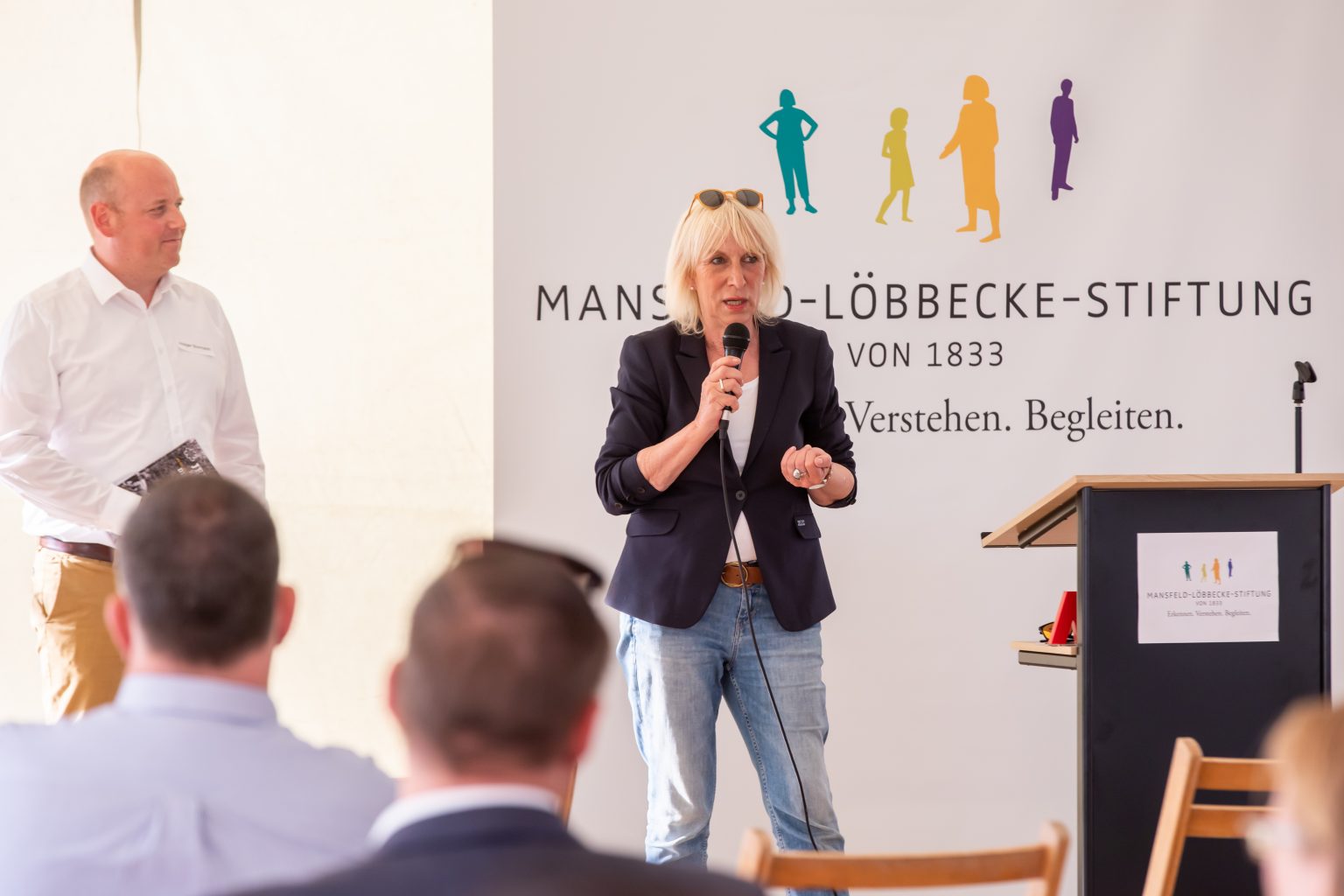 Frau hält Rede vor Mansfeld-Löbbecke-Stiftung Publikum. Veranstaltung, Rednerin, Mikrofon, Stiftung, Zuhörer, Präsentation.