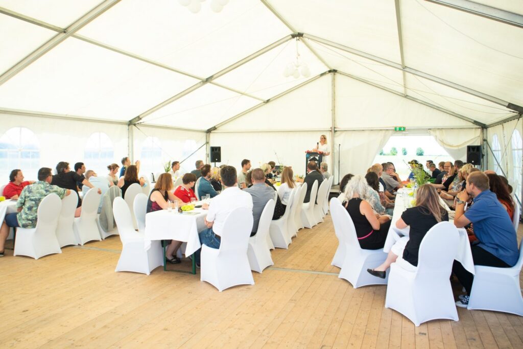 Festzelt Veranstaltung: Menschen sitzen an Tischen, eine Rednerin hält eine Rede bei einer Feierlichkeit.