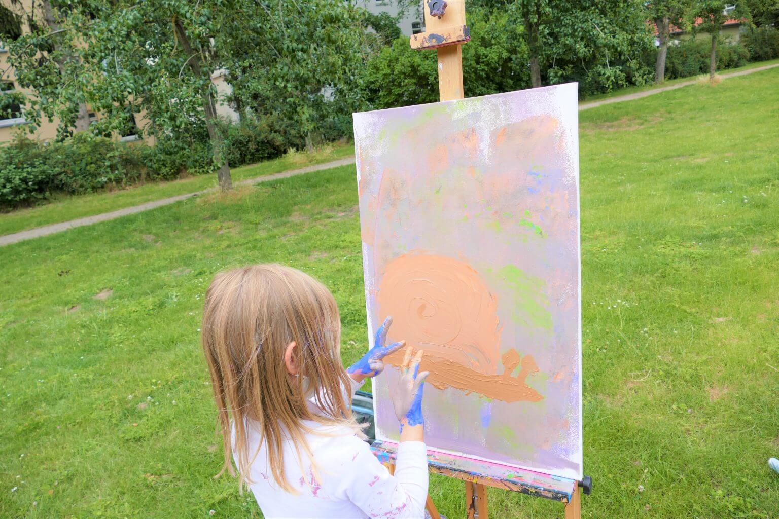Mädchen malt Schnecke mit Fingerfarben auf Leinwand im Park. Kreative Freizeitbeschäftigung für Kinder im Freien.