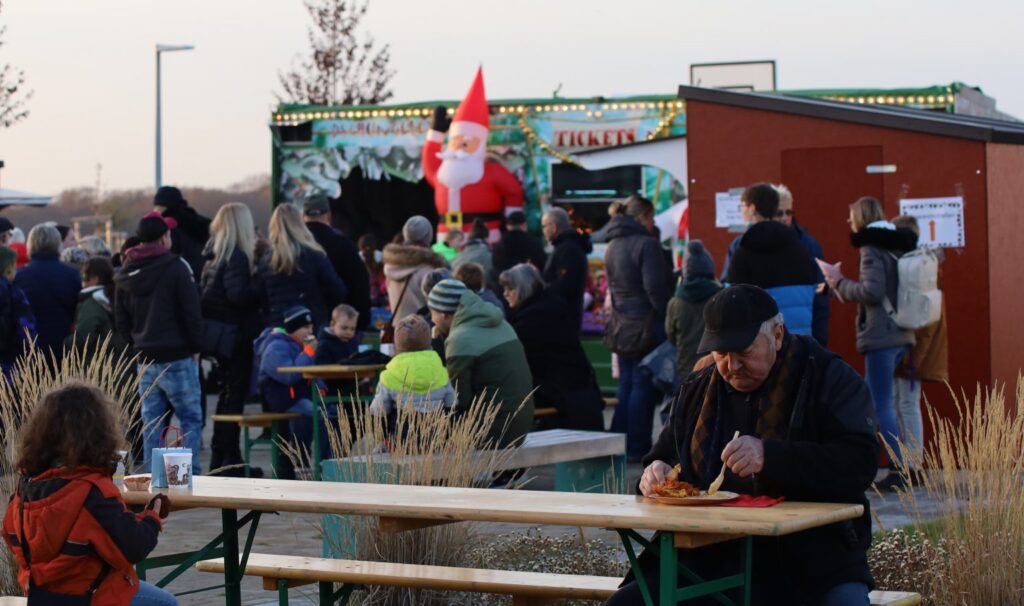 Eine Gruppe von Menschen feiert auf einem Weihnachtsmarkt mit dem Weihnachtsmann.