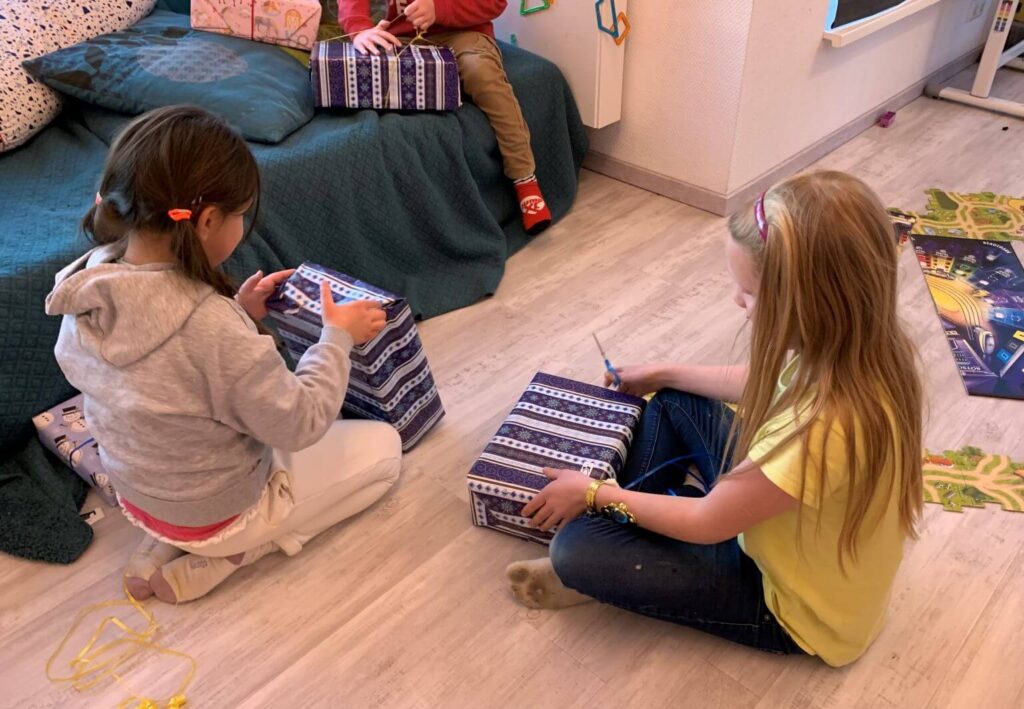 Kinder packen Weihnachtsgeschenke aus. Mädchen mit Schere und Geschenkpapier. Weihnachten, Familie, Freude.