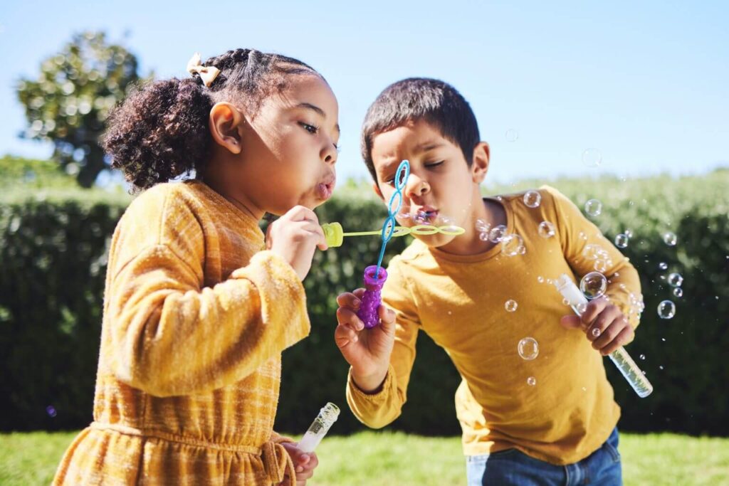 Zwei Kinder pusten Seifenblasen im Garten. Spaß im Freien, Kindheit, Spiel, Sommer, Freundschaft, Freizeitaktivität, Kindergeburtstag.
