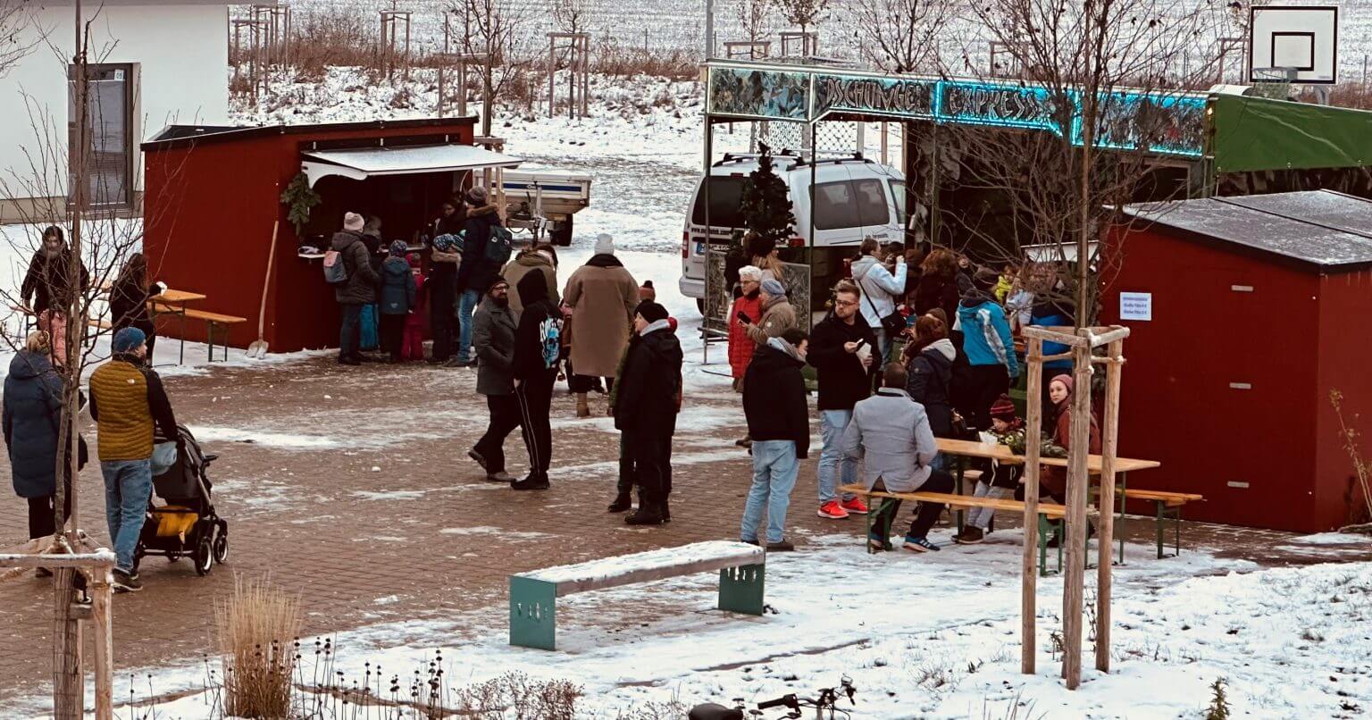 Winterlicher Weihnachtsmarkt: Menschen an Buden, Imbissständen und Karussell. Schnee bedeckt den Boden. Festliche Stimmung.