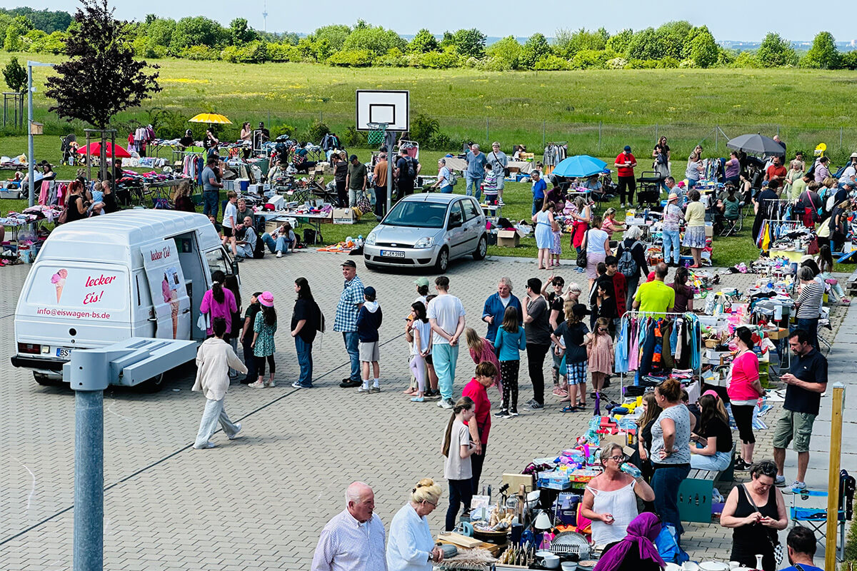 Eine große Gruppe von Menschen steht in einem Parkplatz und unterhält sich miteinander.