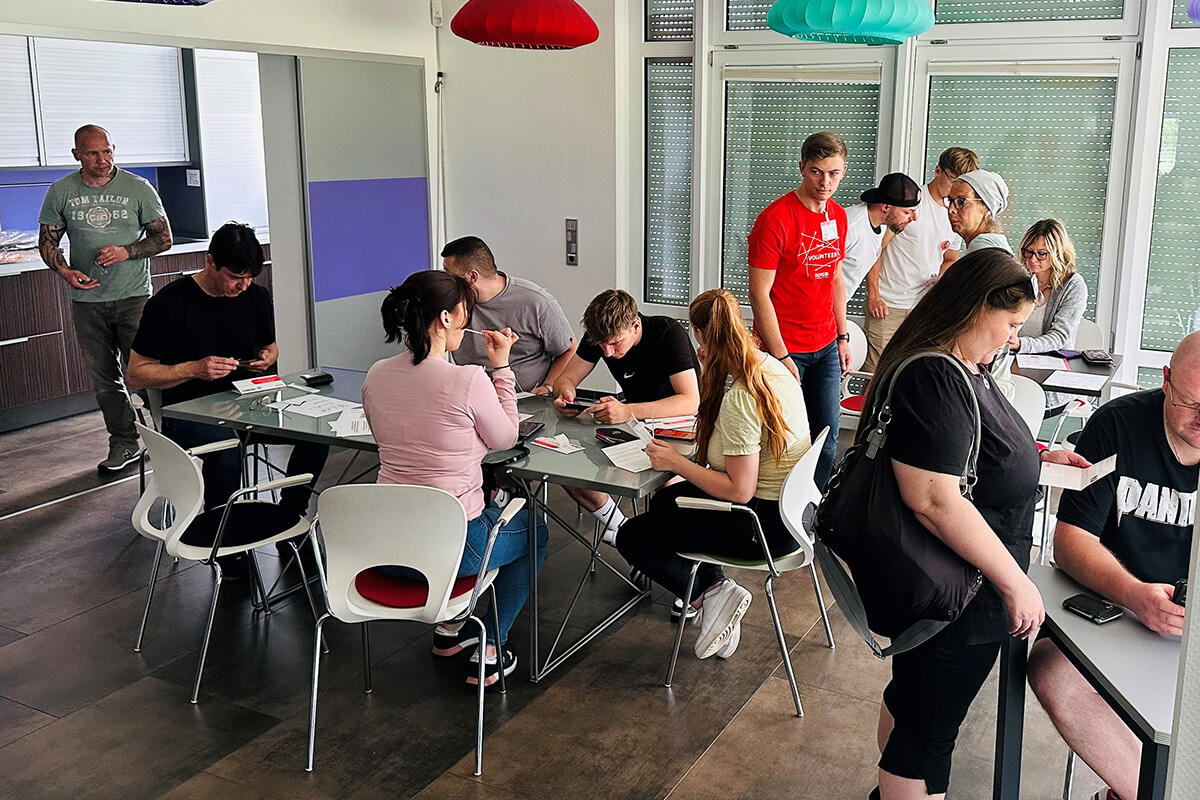 Eine Gruppe von Menschen sitzt an Tischen in einem Raum und führt Gespräche.