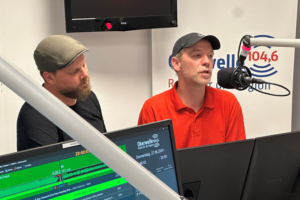 Zwei Männer in einem Studio mit Mikrofonen, die aktiv an einer Radiosendung teilnehmen.