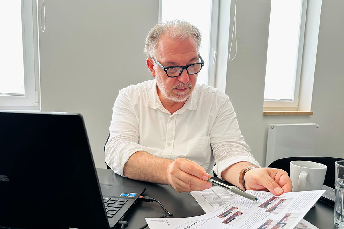 Ein Mann mit Brille und weißem Hemd schaut auf Dokumente.