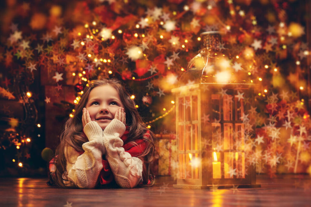 Ein Mädchen liegt auf dem Boden, spielt mit einer Laterne und ist von bunten Weihnachtslichtern umgeben.