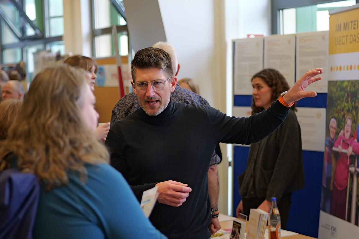 Messebesuch: Mann im Gespräch mit Besuchern an einem Informationsstand, Beratung und Austausch im Fokus.