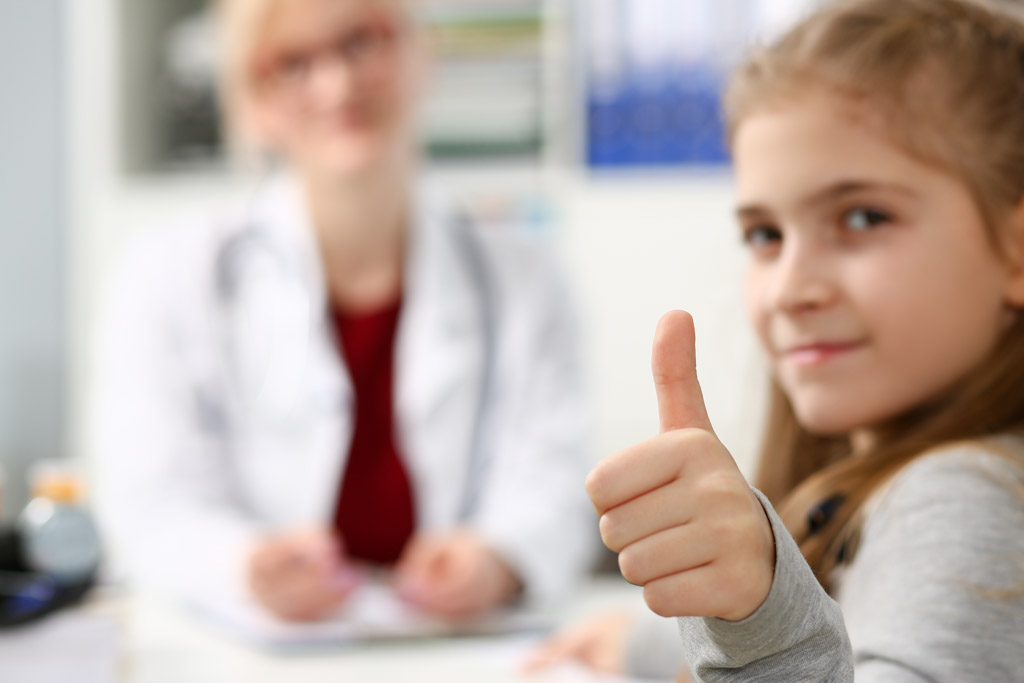 Ein kleines Mädchen lächelt und zeigt den Daumen hoch, was Zustimmung und Freude symbolisiert.