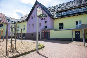 Ein Gebäude mit einem Spielplatz im Vordergrund, umgeben von Bäumen und Rasenflächen.