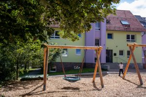 Spielplatz mit Schaukeln und einer Schaukelkonstruktion vor einem Gebäude.