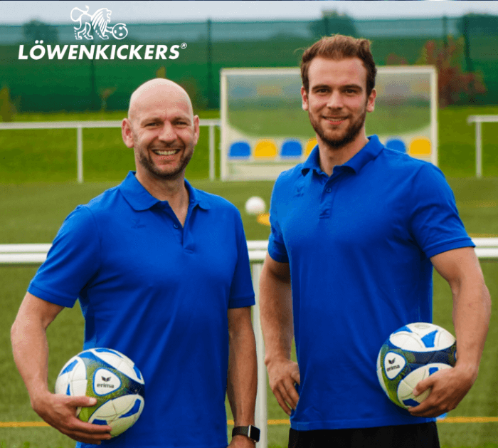 Zwei Männer in blauen Hemden halten Fußballbälle in den Händen.